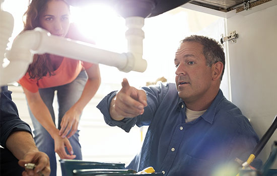 plumber working on pipes under sink