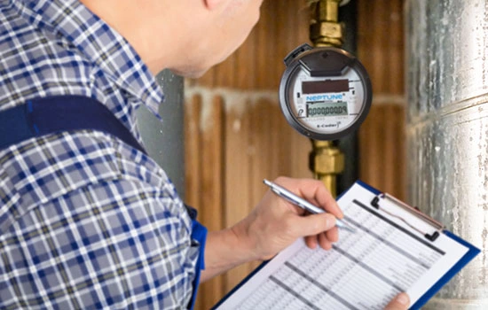 Utility worker in plaid shirt recording meter reading on clipboard while checking water meter gauge