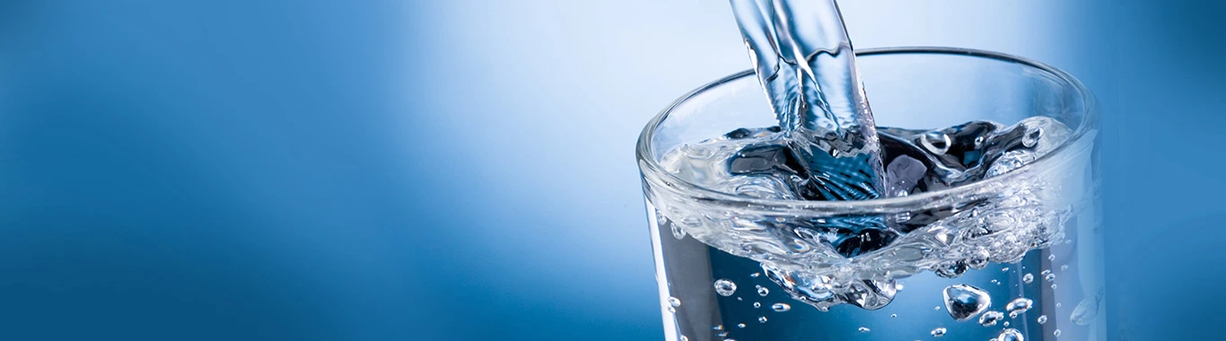 Water pouring into a glass with ice cubes against a blue background