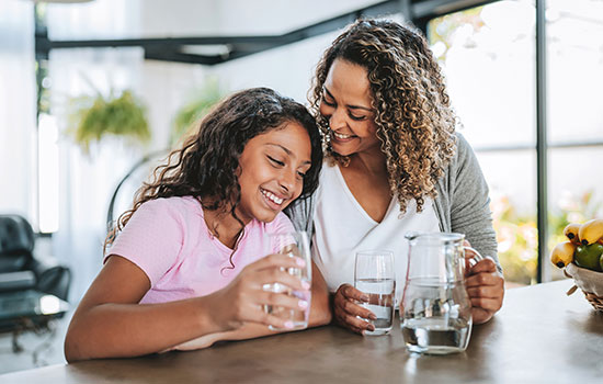 mother and daughter smiling at kitchen table while holding glasses of water